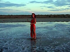 Mature woman strolls outdoors by Elton Salt Lake at red sunset with small tits exposed