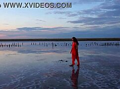 Mature woman strolls outdoors by Elton Salt Lake at red sunset with small tits exposed