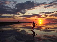 Mature woman strolls outdoors by Elton Salt Lake at red sunset with small tits exposed