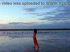 Mature woman strolls outdoors by Elton Salt Lake at red sunset with small tits exposed