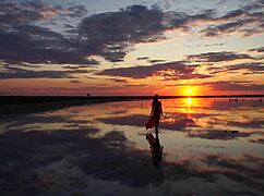 Mature woman strolls outdoors by Elton Salt Lake at red sunset with small tits exposed