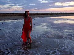 Mature woman strolls outdoors by Elton Salt Lake at red sunset with small tits exposed